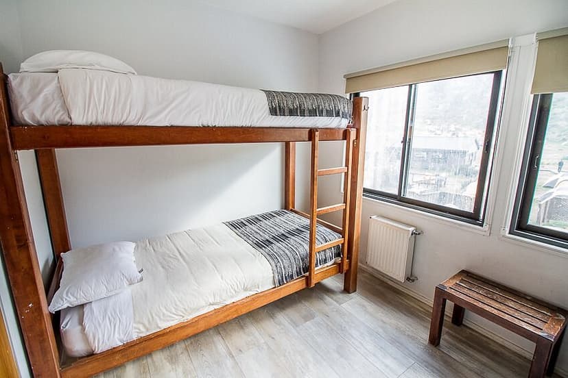 Wooden bunk beds with white bedding in a room with a window view of Refugio Vertice Paine Grande.