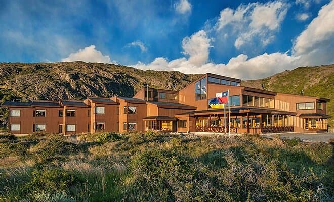 Refugio Vertice Paine Grande lodge in rugged landscape under a blue, cloudy sky.