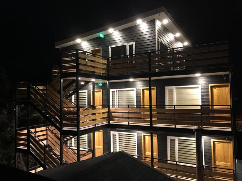Modern three-story building with black siding, wood railings, and external stairs at night in Patagonia.