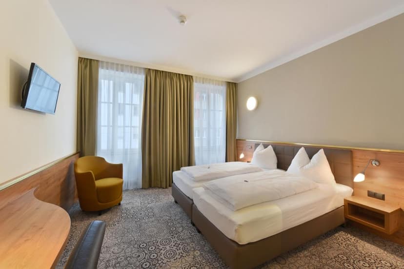 Hotel room with twin beds, yellow armchair, wall-mounted TV, and patterned carpet