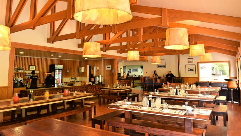 Rustic dining hall with wooden beams, long tables, and bar service area.