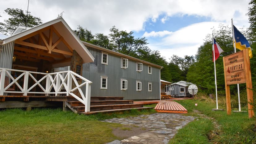 Refugio & Camping Grey welcome sign with Chilean flag, set among green trees.