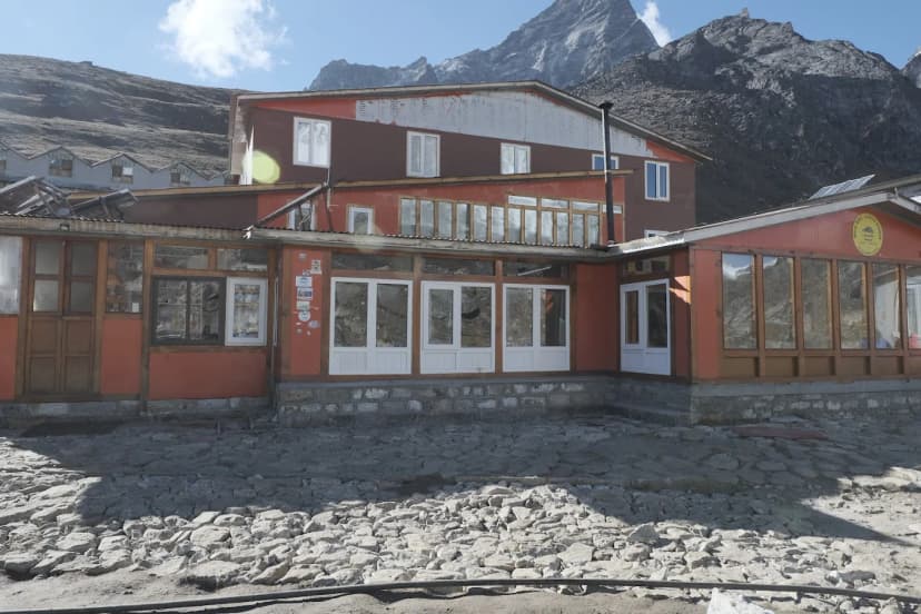 Hotel New EBC Lobuche guesthouse with rocky foreground and steep mountains under blue sky.