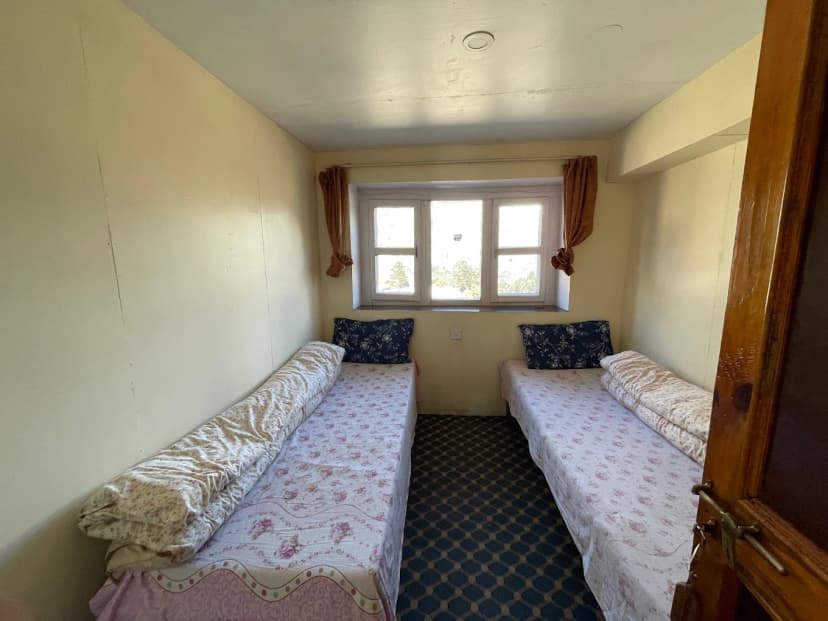 Twin beds in a simple room with a window view at Himalayan Hotel Tengboche