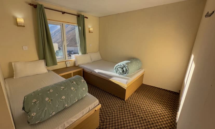 Twin room in Hotel Dingboche with mountain view through window and floral rolled duvets.