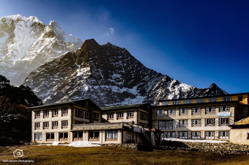 Himalayan Hotel Tengboche against massive snow-capped Himalayan mountains under a bright blue sky.