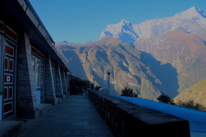 Lodge walkway with stone pillars overlooking massive, sunlit Himalayan mountains near Namche Bazaar.