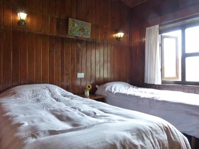 Twin beds in a wood-paneled room with bright window light at Airport Resort Lukla.