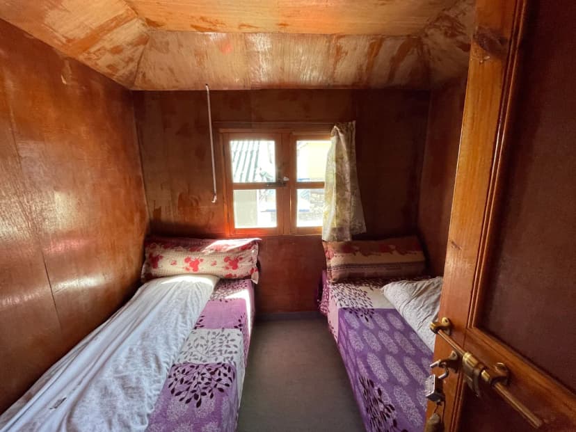 Twin beds inside a small room with wood paneling and a window at Buddha Lodge Gorakhshep.