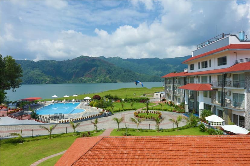 Waterfront resort with pool, lake, and green mountains; paraglider visible. KGH Group Pokhara.