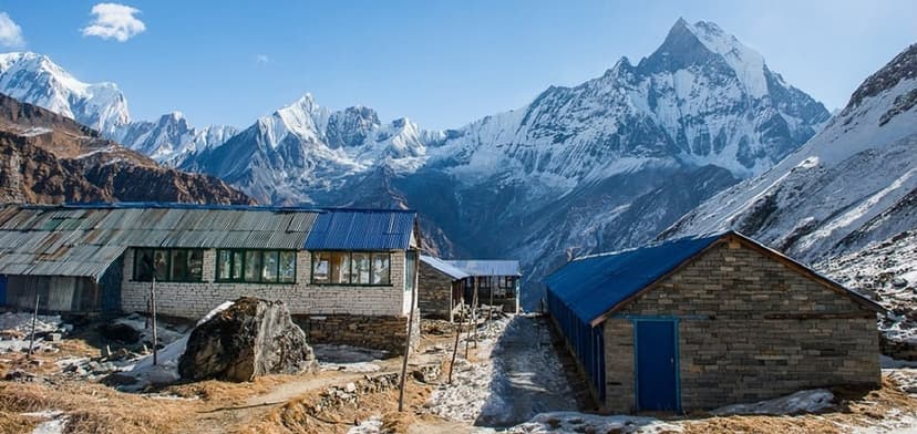 Annapurna guesthouse buildings in a high mountain valley with snow-capped peaks under a blue sky.