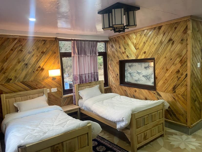 Twin beds with white linens in a room with diagonal wood paneling at The Sunny Hotel Ghorepani.