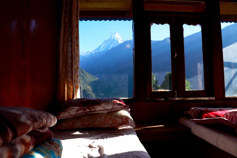 Simple guesthouse room with beds and a window view of Annapurna mountain peaks.