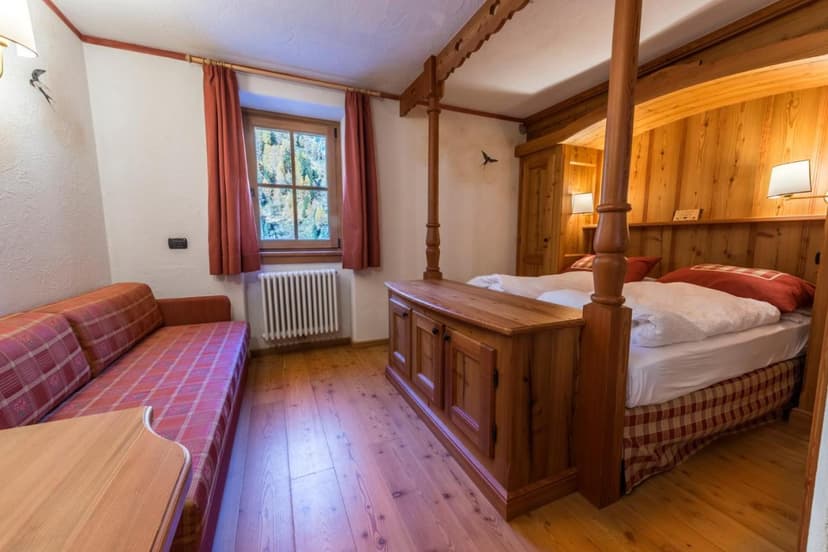 Cozy wooden bedroom with four-poster bed and plaid sofa, alpine view from window
