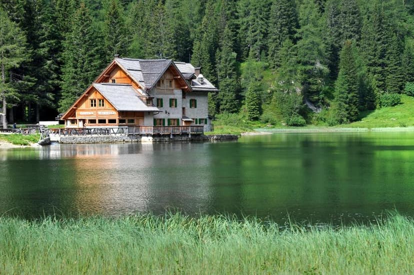 Lakeside alpine lodge with wooden balconies reflected in green water, surrounded by pine forest.