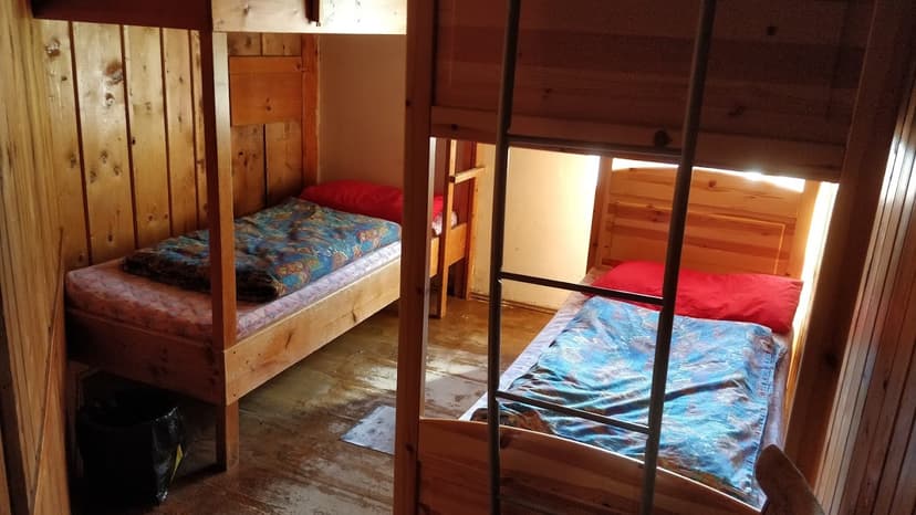 Wooden bunk beds and single beds with colorful blankets inside a rustic mountain hut.