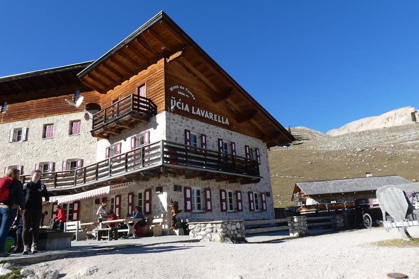 Rifugio Ucia Lavarella stone mountain hut with wooden balconies under clear blue sky.