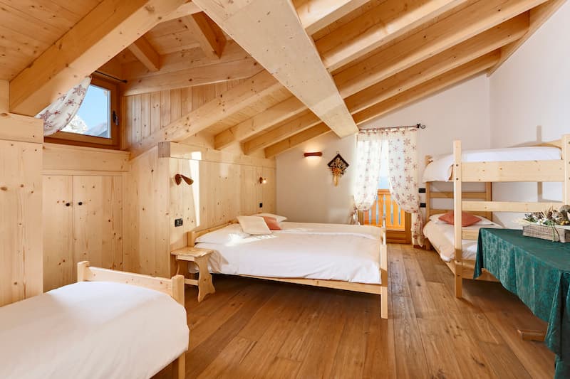 Attic bedroom with wood paneling, double bed, bunk beds, and view of snowy mountains from Rifugio Averau.