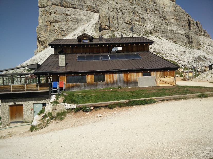 Rifugio Averau mountain hut with wooden exterior against massive rocky Dolomites cliff face.
