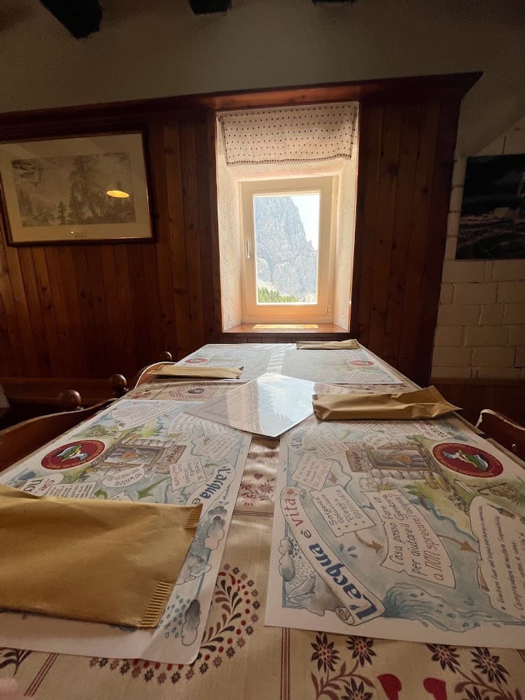 Dining table set inside Rifugio Citta di Fiume with mountain view through window.