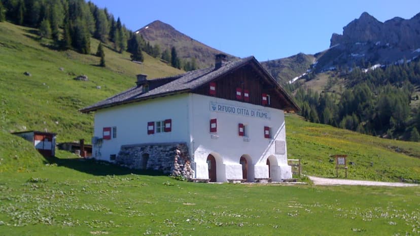 Rifugio Citta di Fiume mountain hut on green hillside with rocky peaks in background