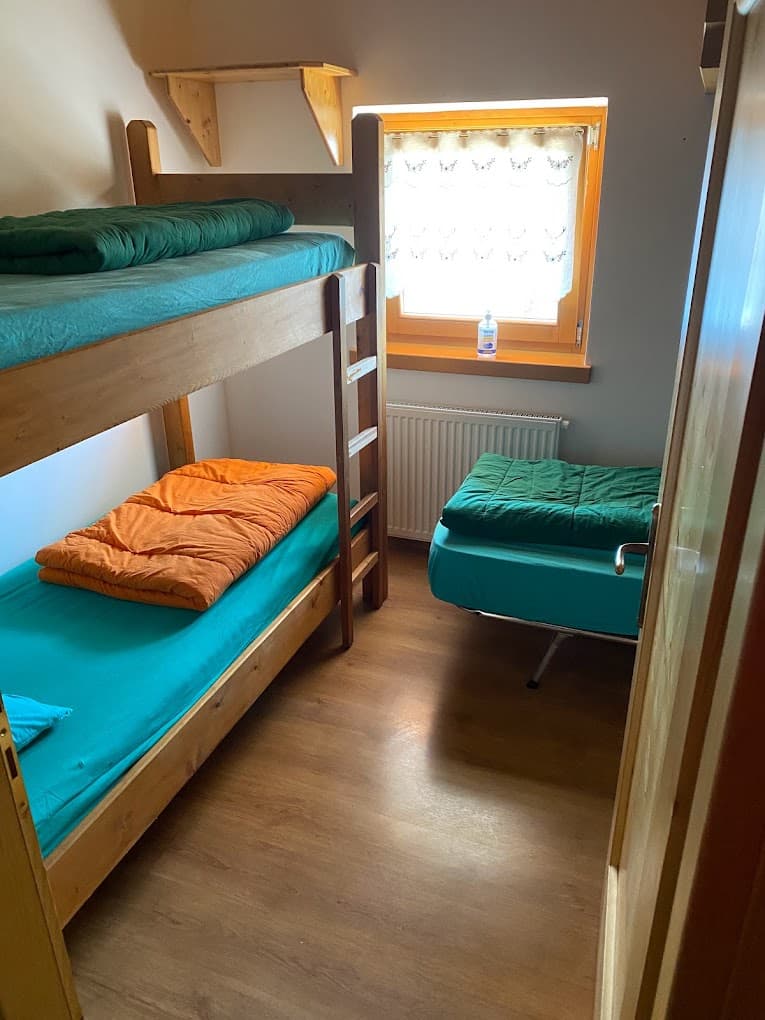 Simple wooden bunk beds and a single bed in a small room with a bright window at Rifugio Carestiato.