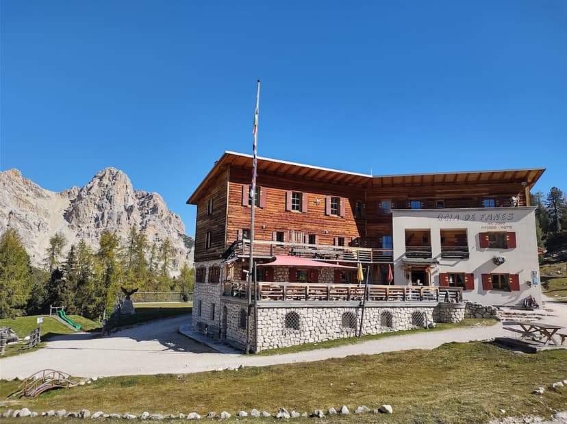 Rifugio Fanes mountain hut with wooden structure against rocky peaks and clear blue sky.