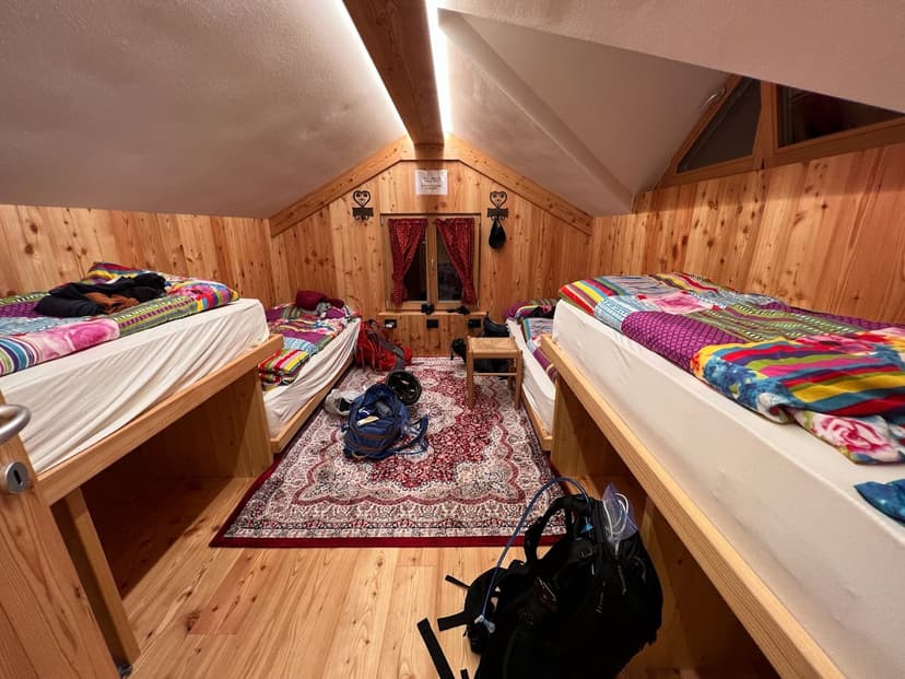 Bunk room interior with wooden walls, colorful bedding, and hiking backpacks at Rifugio Passo Staulanza.