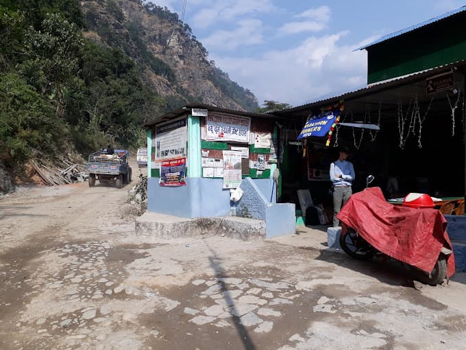 Roadside buildings and information board near a dirt road with a truck in a mountainous, forested area.