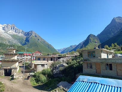 Village buildings nestled in a valley surrounded by steep, green and snow-capped mountains under a clear blue sky.