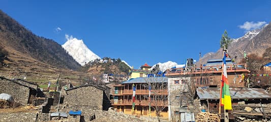 Mountain village with stone houses, colorful guesthouse, and snow-capped peaks under blue sky in Lho.