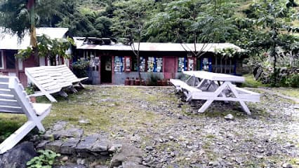 Guest house entrance with white wooden benches and picnic table on gravel ground near forest.