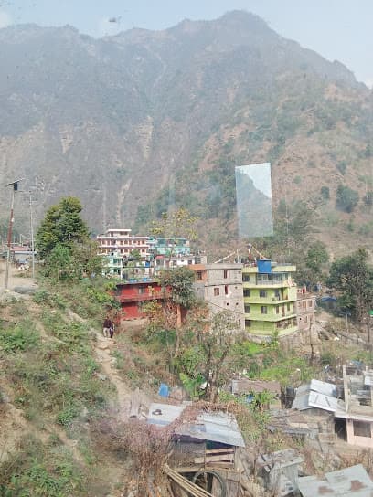Colorful buildings nestled on a steep hillside below large, hazy mountains at Hotel Hilltop Macchakola.