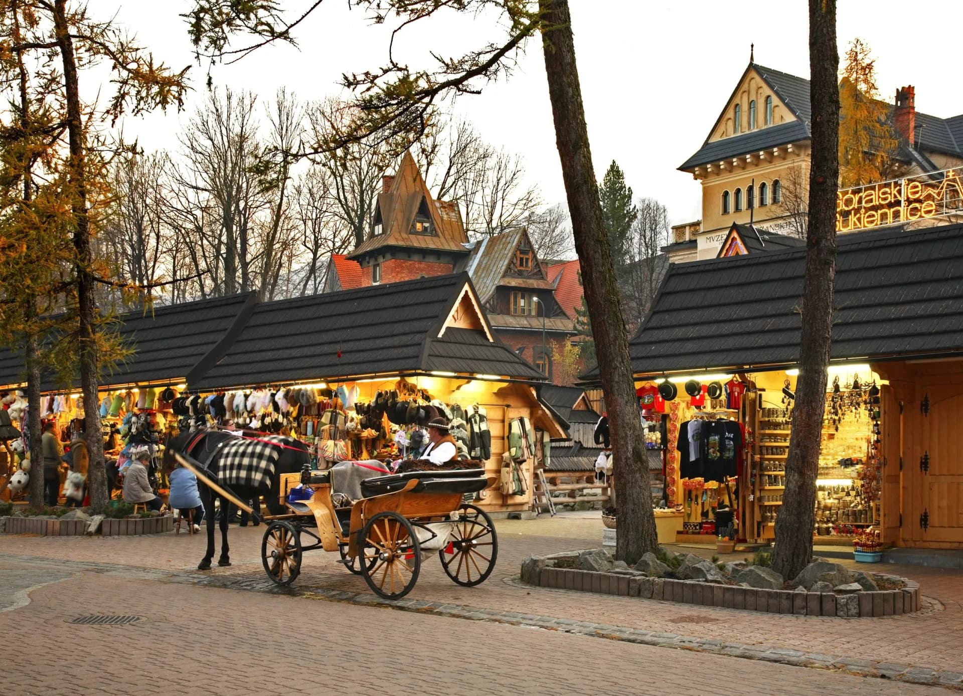 Horse-drawn carriage near illuminated wooden market stalls in Zakopane, Poland with Tatras architecture.