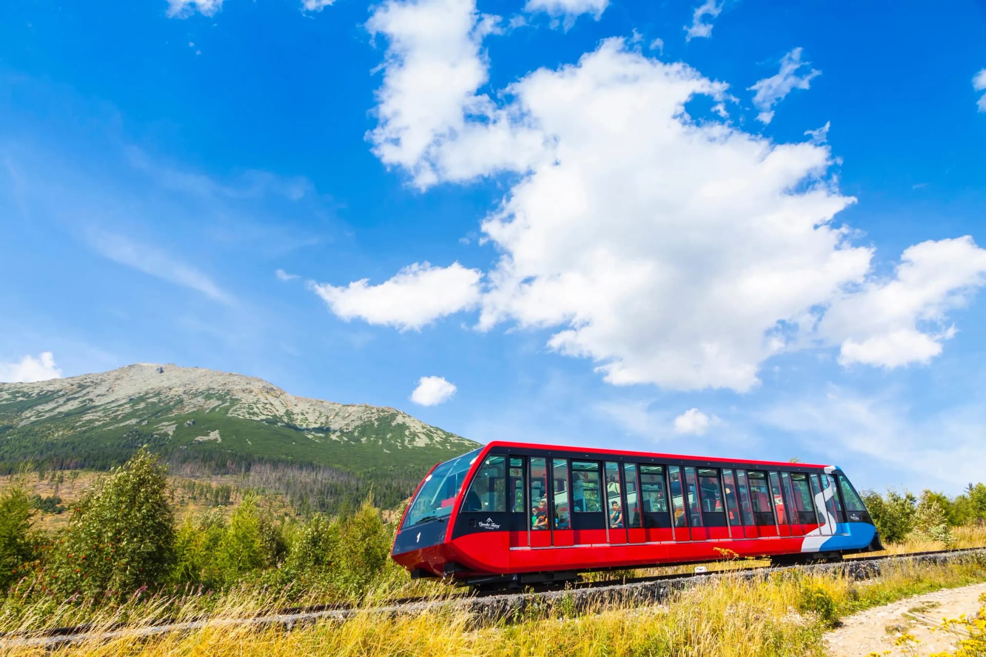 Red funicular train traveling through grassy mountainside under a bright blue sky in the Tatras.