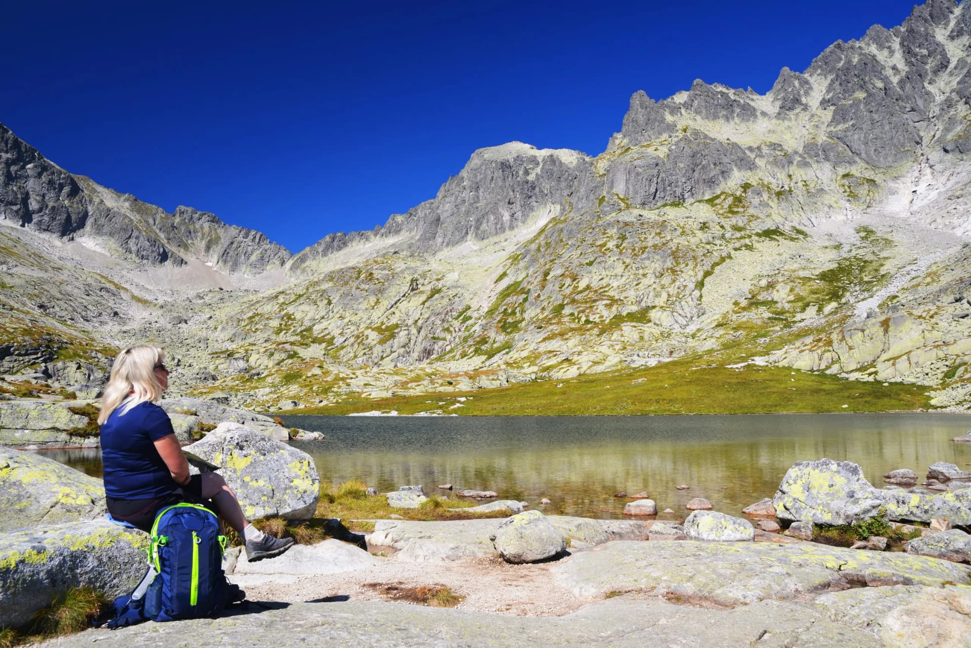 Hiker resting by mountain lake with rocky slopes and clear blue sky, Mala Studena Dolina.