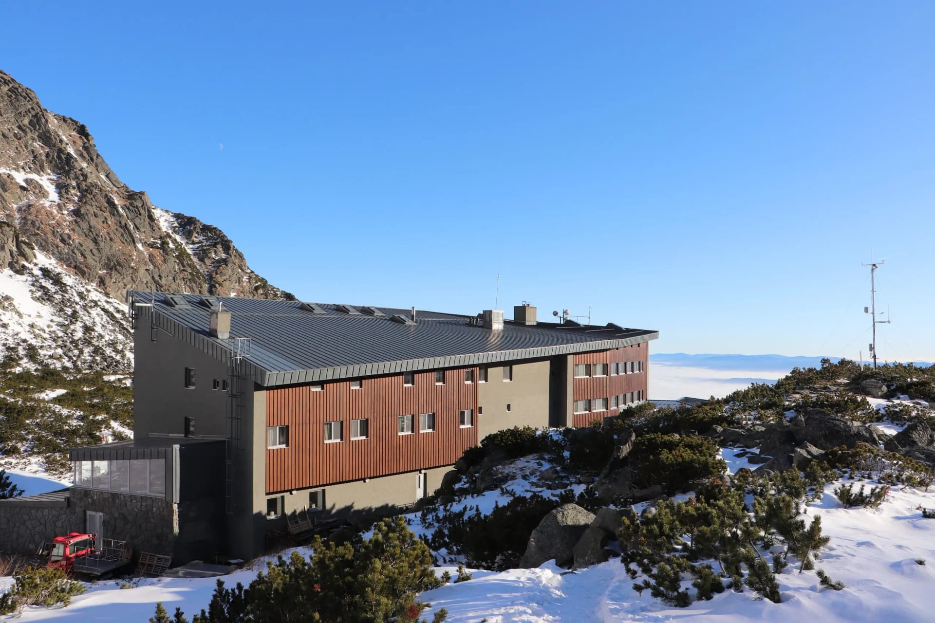 Mountain refuge building in snow with rocky terrain and clear blue sky, Tatras.