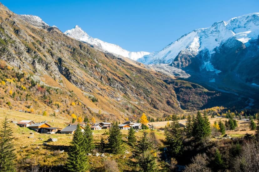 Alpine village nestled in valley with steep slopes and snow-capped mountains in autumn