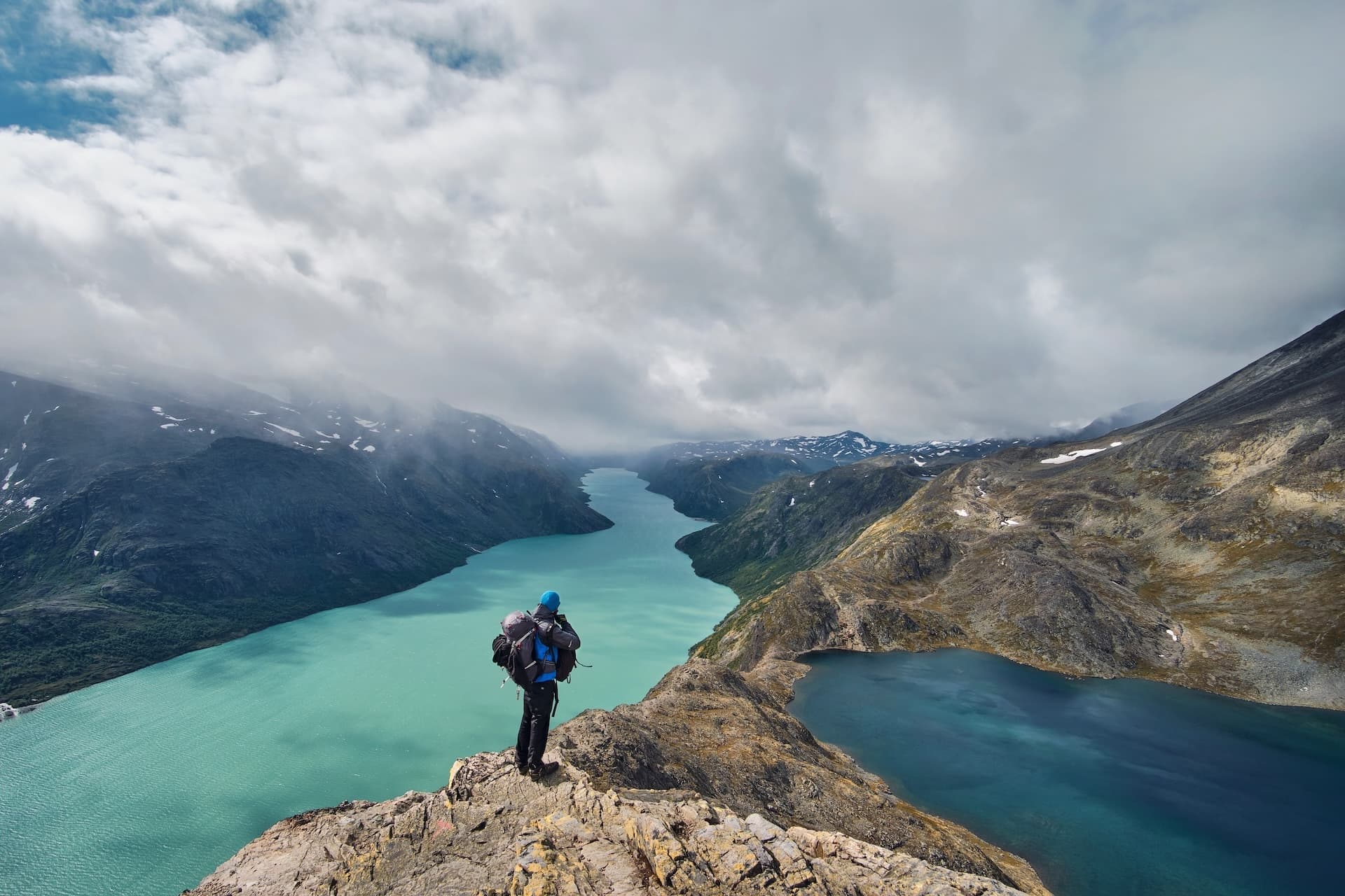 Hiker with backpack overlooking turquoise glacial lake and valley from Besseggen Ridge.