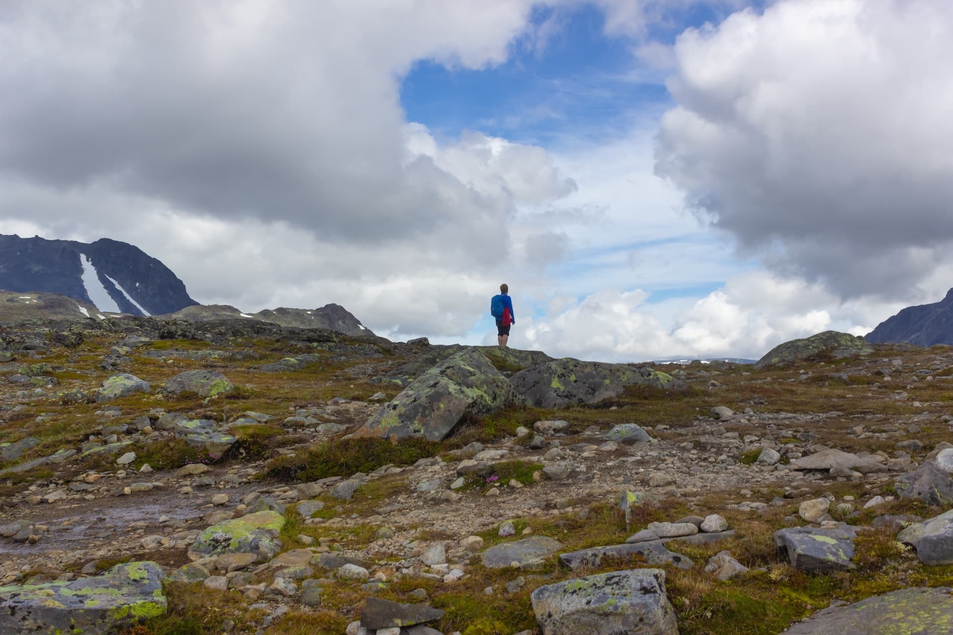 Hiker standing on rocky plateau with Besseggen ridge mountains and cloudy sky.