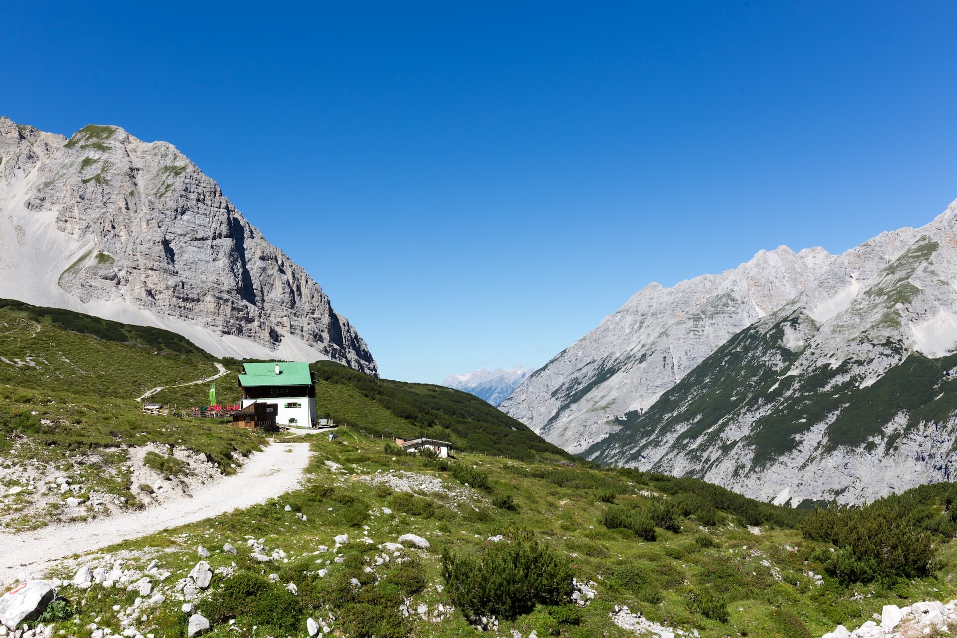 Alpine hut with green roof on grassy slope between steep grey mountains above Innsbruck.