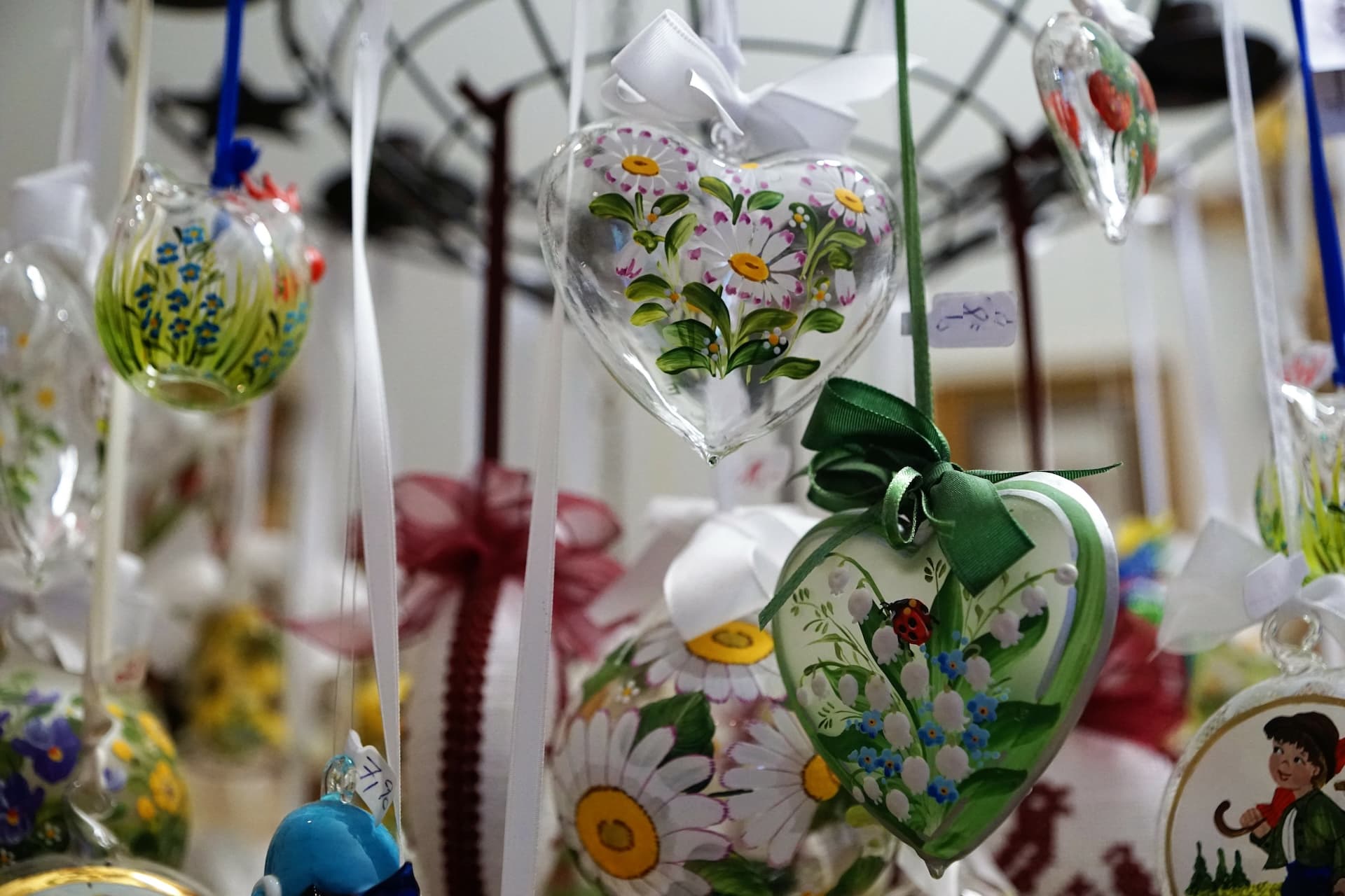 Hand-painted glass heart souvenirs with flowers and ladybugs hanging in Innsbruck shop.