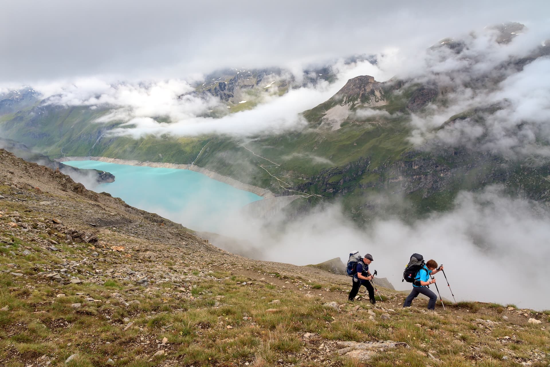 Hikers with backpacks ascend rocky terrain above Lac de Moiry reservoir in Switzerland.