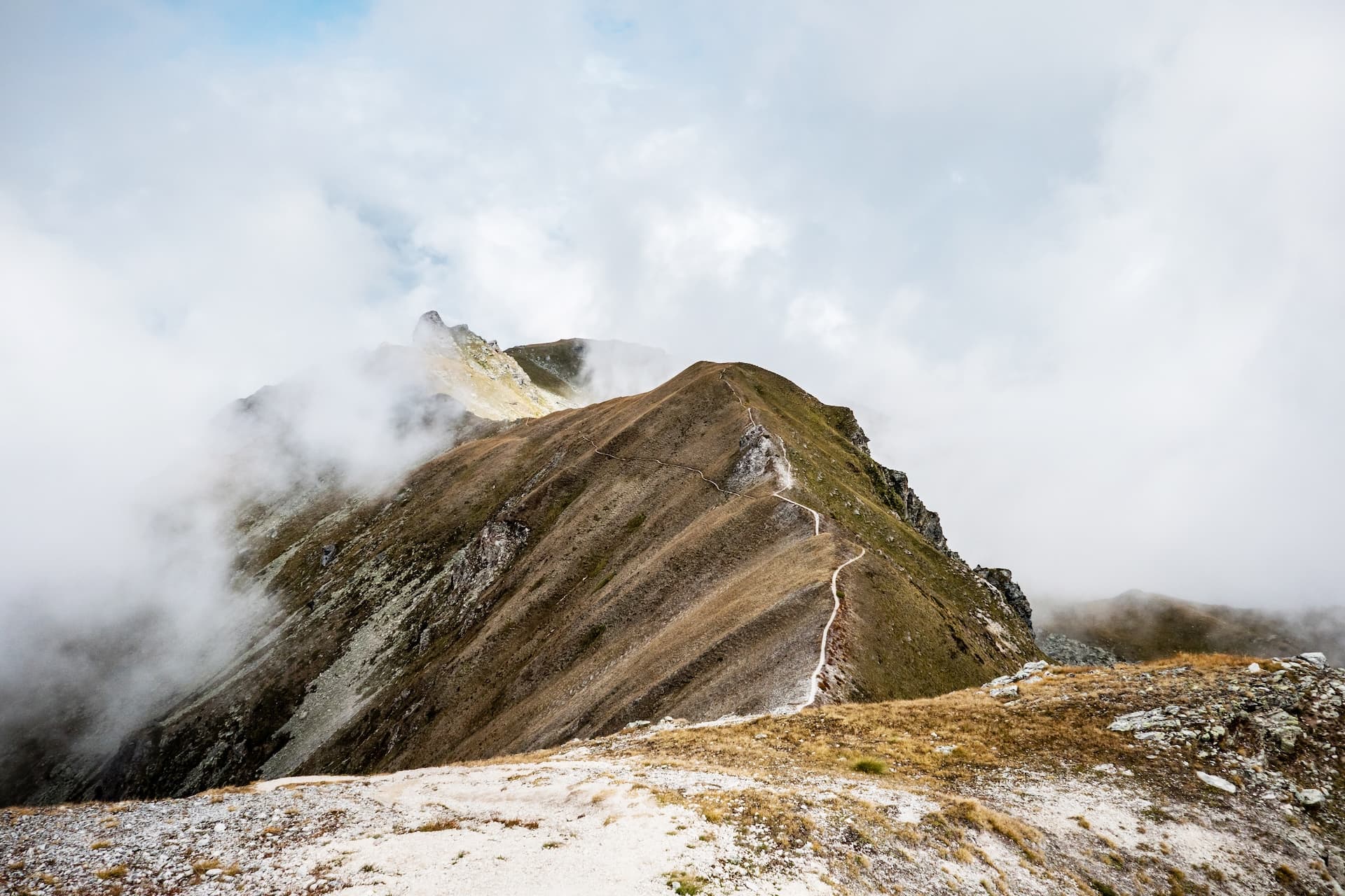 Hiking trail along a grassy mountain ridge partially obscured by low clouds and fog.