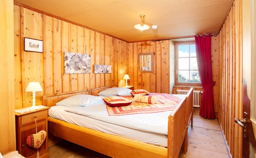 Cozy hotel bedroom with wood paneling, a wooden bed, and a window showing clouds and mountains.