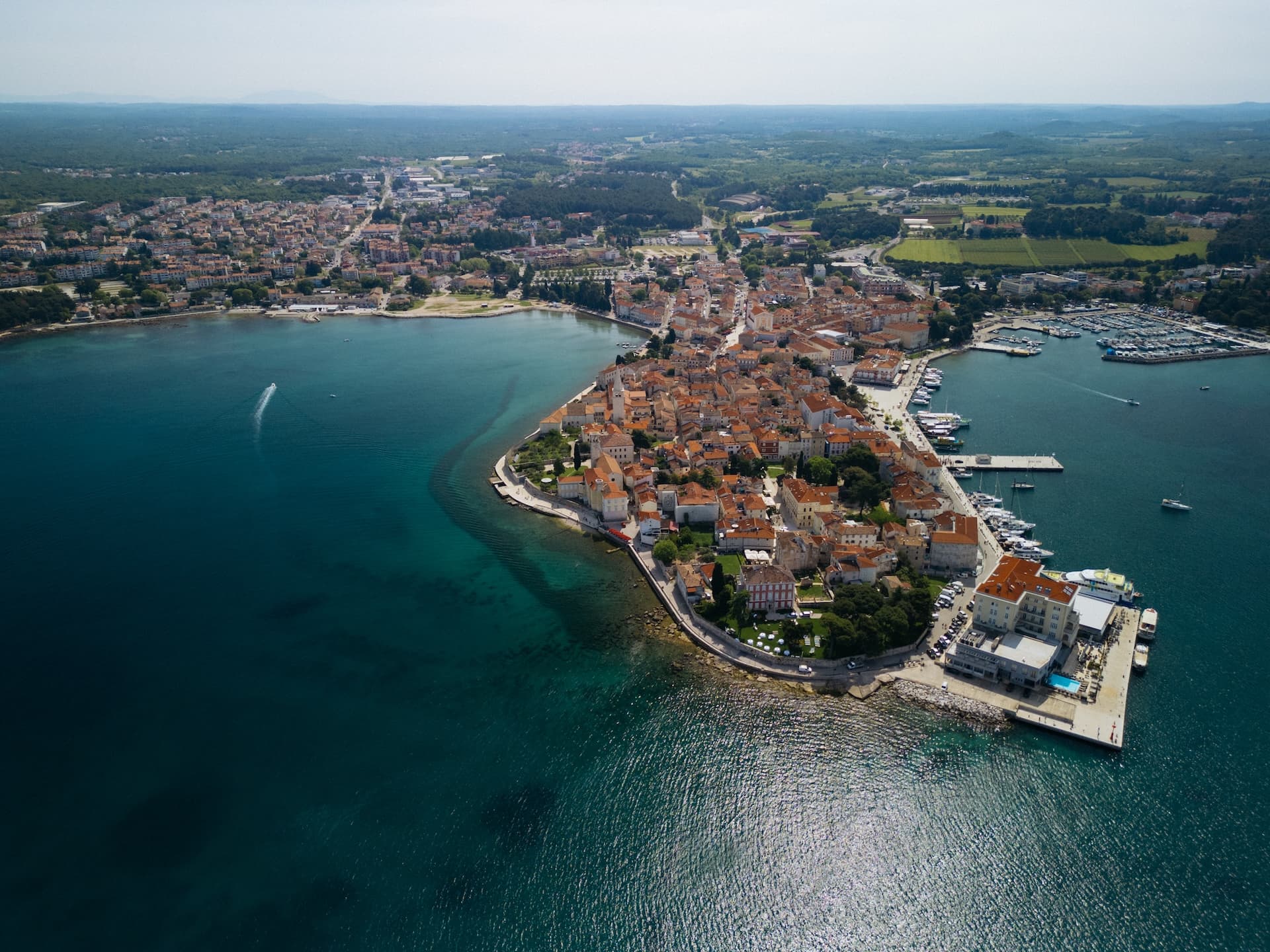 Aerial view of historic town with terracotta roofs on Istrian coast peninsula with marina and turquoise sea.