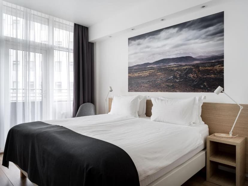 Hotel room with white bedding, dark throw, and large volcanic landscape art above the bed.
