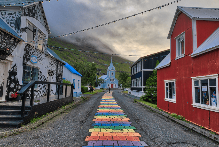 Rainbow path leading to a blue church between colorful buildings in Reykjavik, Iceland.