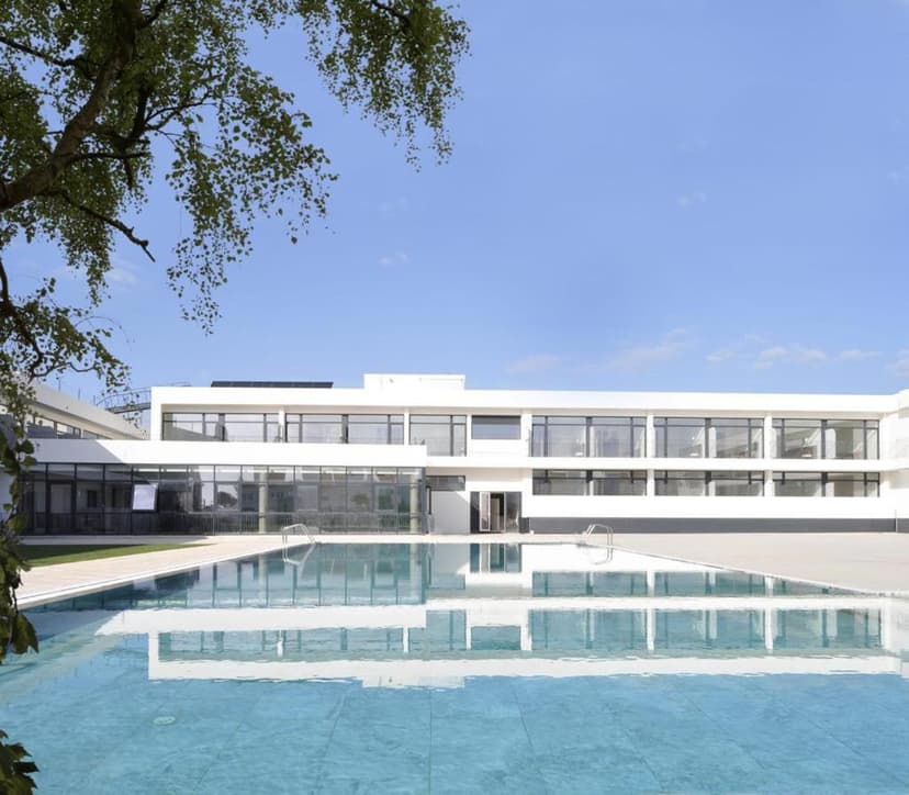 Modern white hotel building exterior with large windows reflected in the outdoor swimming pool at Porto Covo Praia Hotel a...