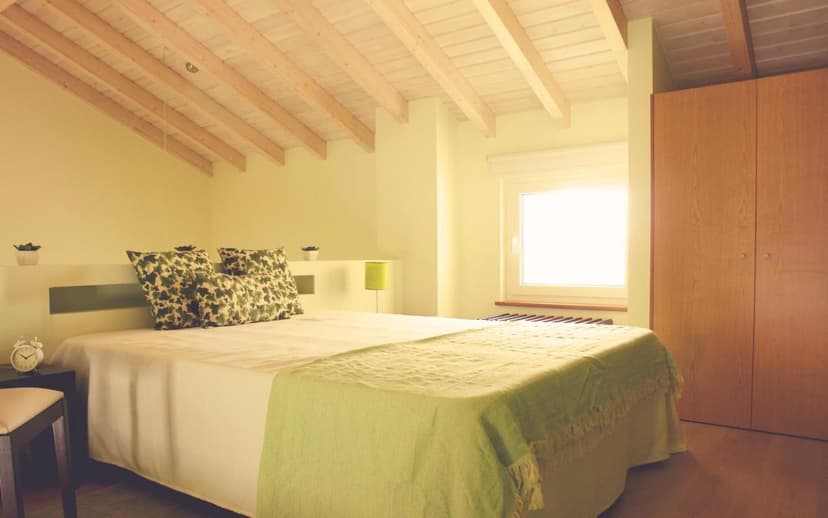 Bedroom with sloped wooden beam ceiling, white bedding, green accents, and bright window.
